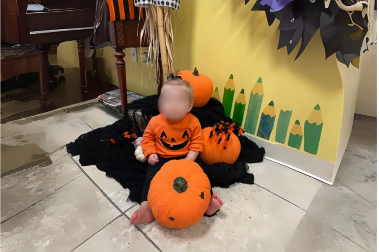Toddler in a pumpkin costume among Halloween decorations