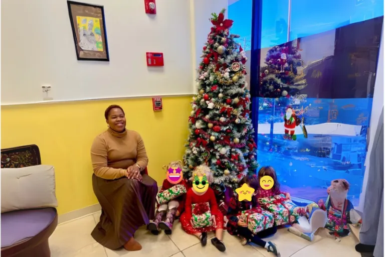 Teacher and children in festive outfits by the Christmas tree