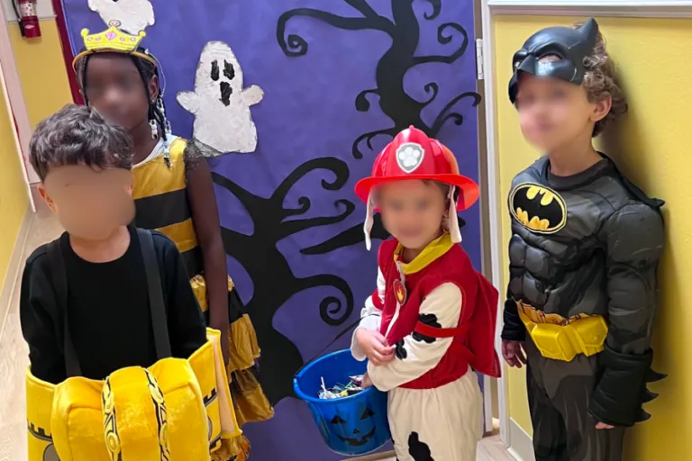 Children in Batman and firefighter costumes by a Halloween door