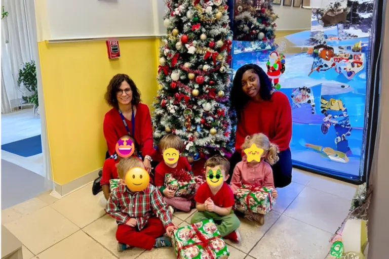 Teachers and children in festive outfits by the Christmas tree