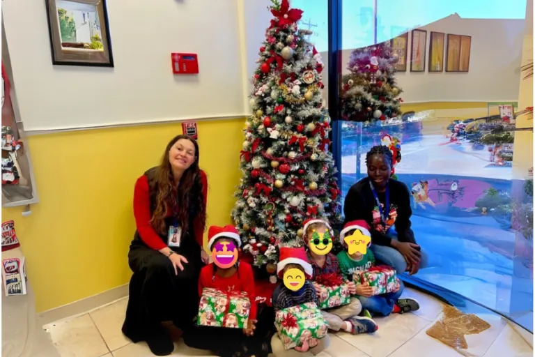 Teachers and children in festive outfits by the Christmas tree