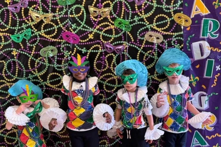 Children in Mardi Gras masks and beads in front of the photo wall